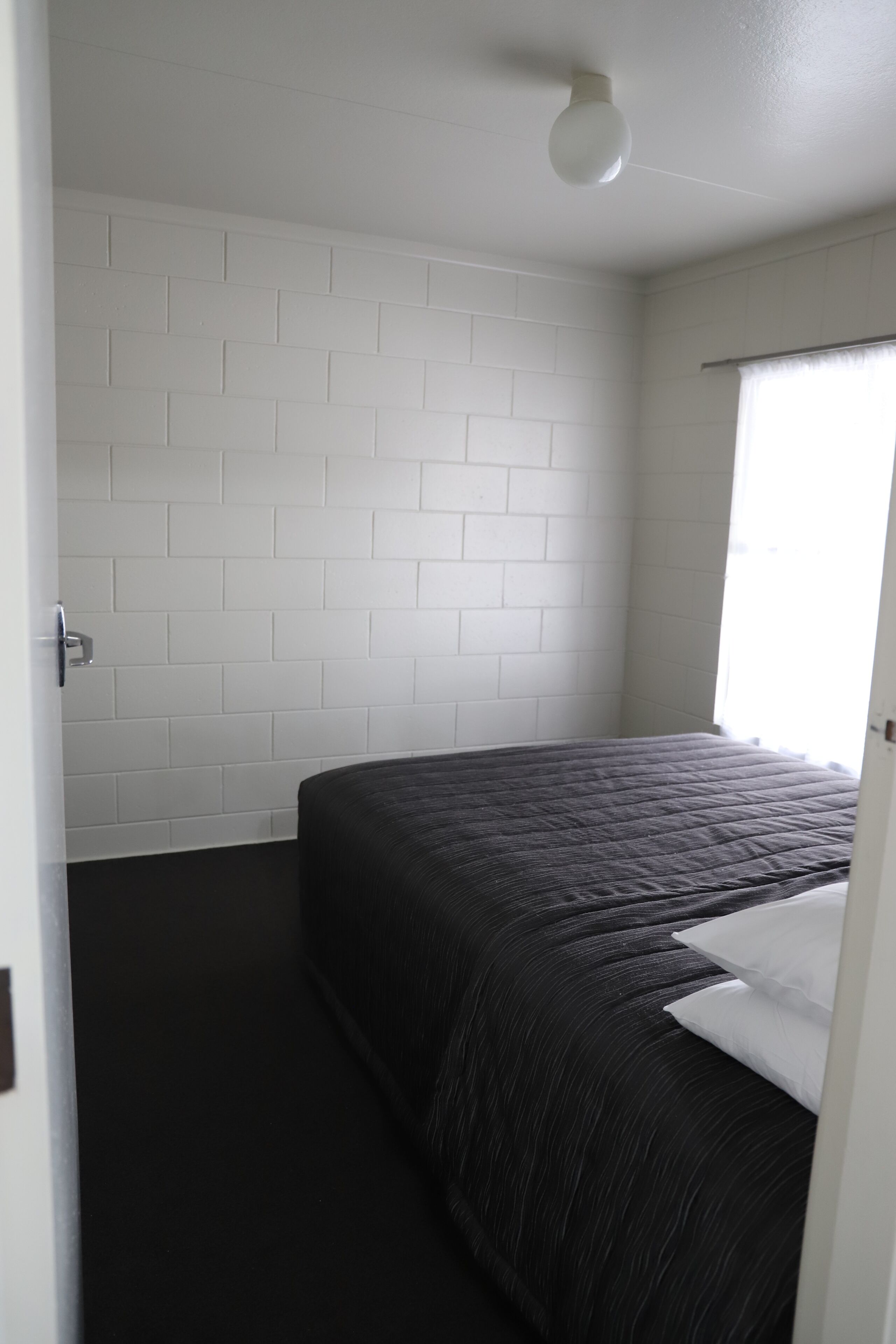 Un dormitorio con cama, pared de ladrillo blanco y ventana con cortinas.