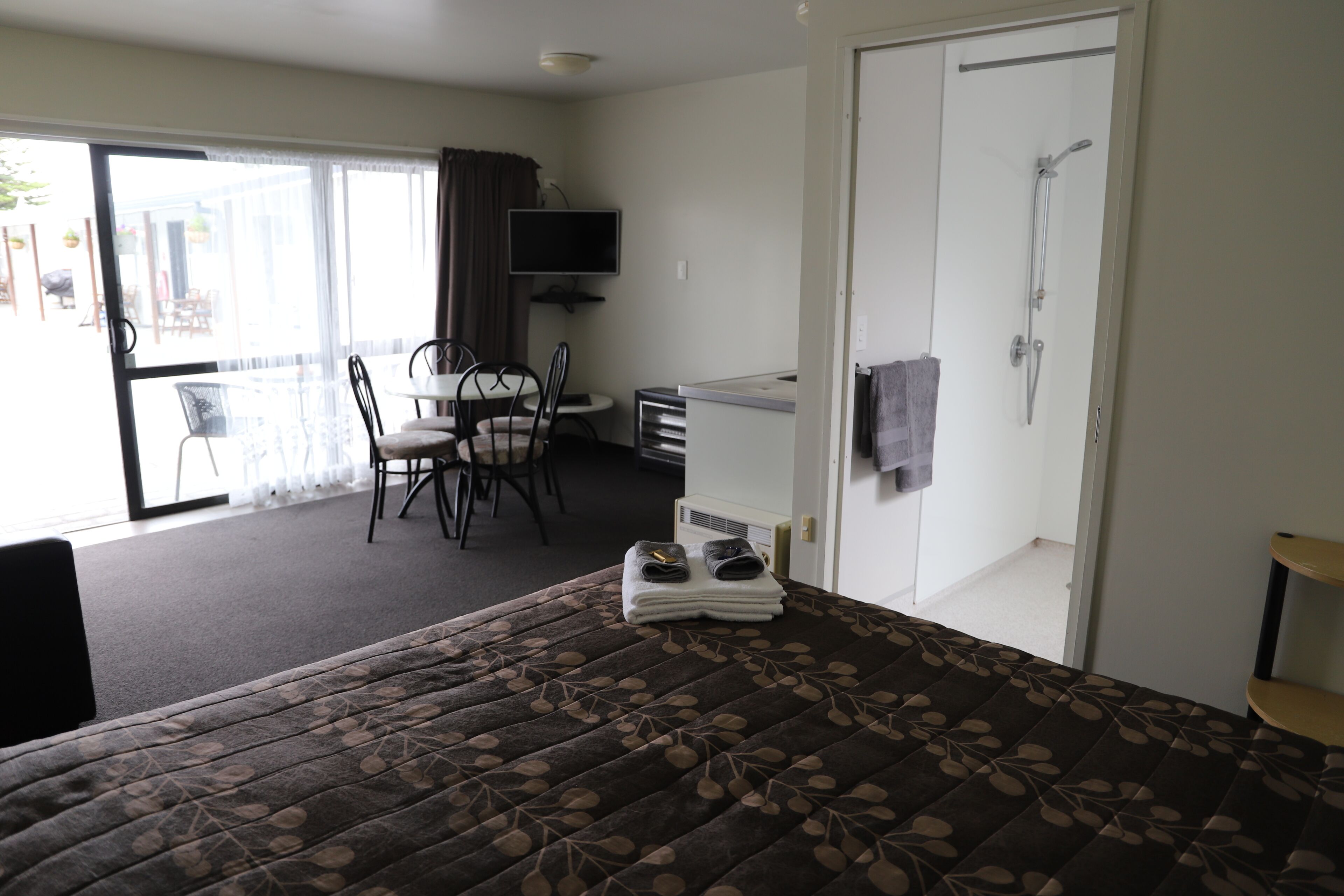 Ett hotellrum med en säng, ett skrivbord, en stol, en tv och en dusch.