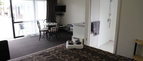 Ett hotellrum med en säng, ett skrivbord, en stol, en tv och en dusch.