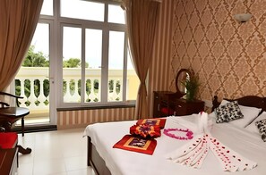 Ein Hotelzimmer mit Bett, Schreibtisch, Stuhl, einem Fenster mit Vorhängen und Blick ins Grüne.