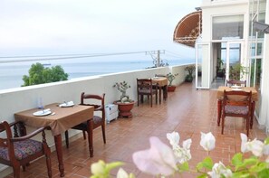 Ein Balkon mit Tisch für zwei Personen, Stühlen, Blumentöpfen und Blick auf das Meer.