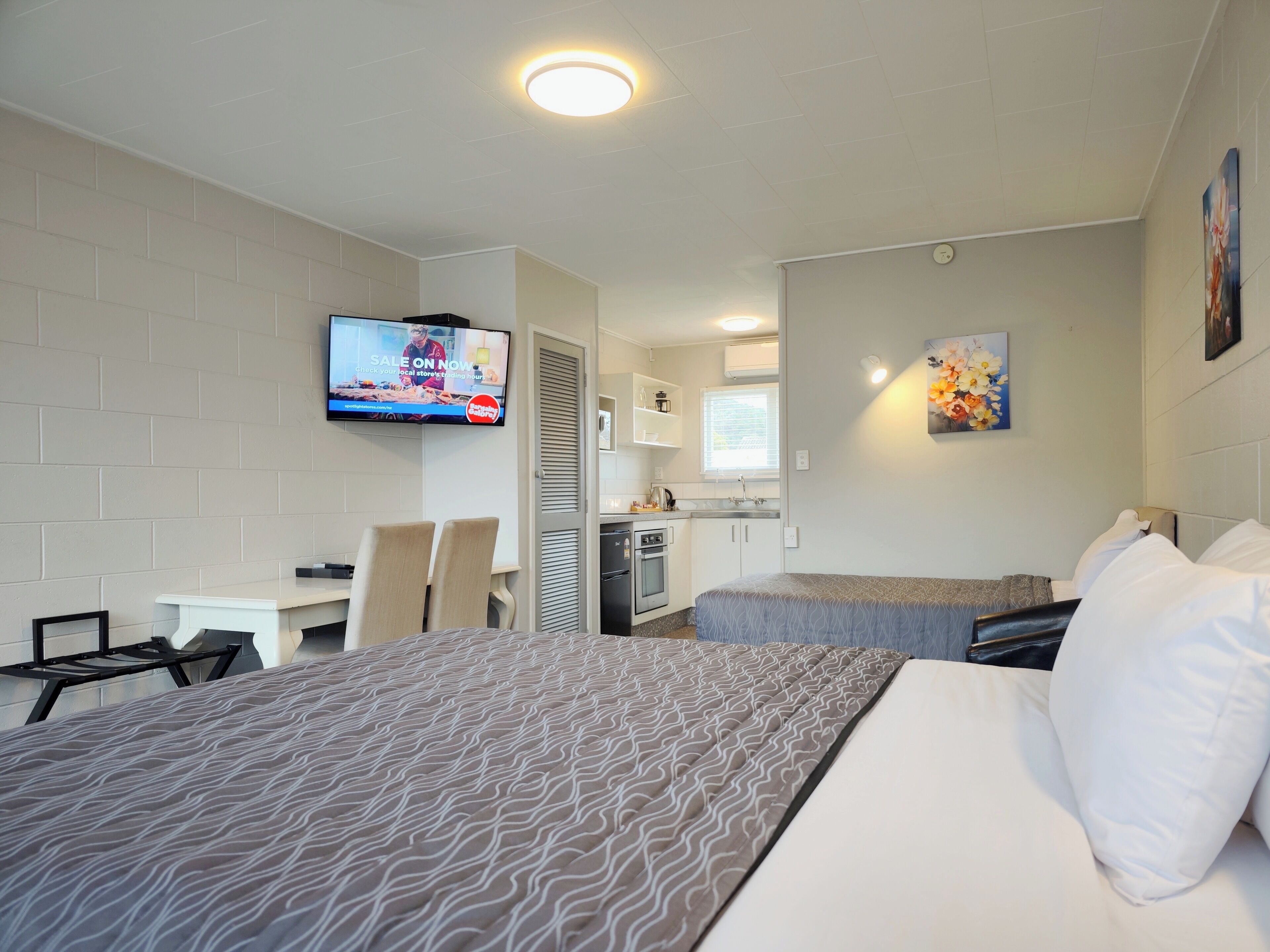 A hotel room with two beds, a TV mounted on the wall, a kitchenette, and a painting on the wall.