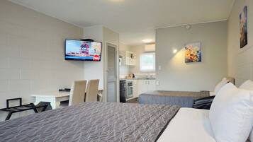 Habitación de hotel con dos camas, un televisor montado en la pared, una kitchenette y un cuadro decorativo.