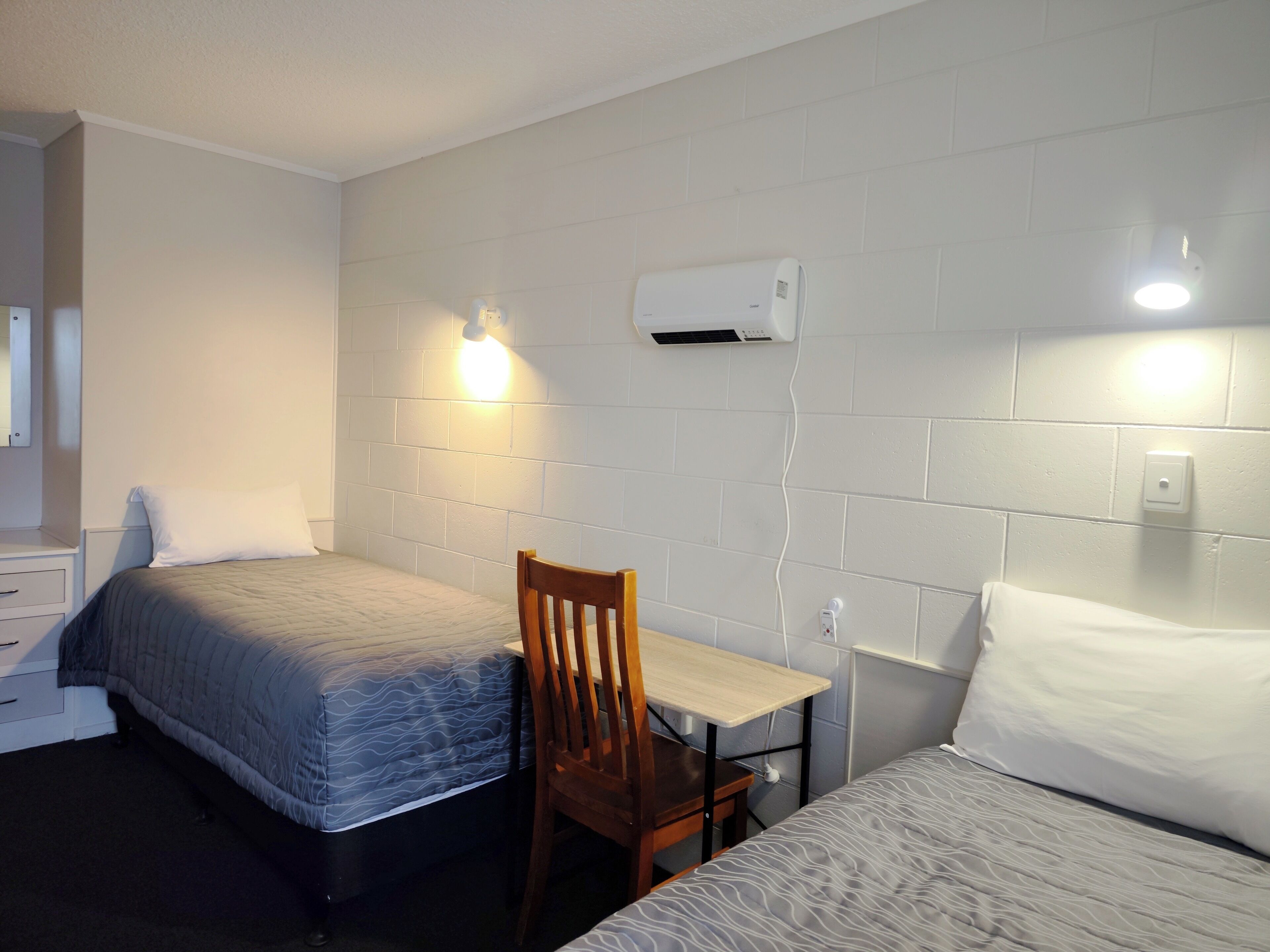 A hotel room with two beds, a desk, and an air conditioning unit mounted on the wall.