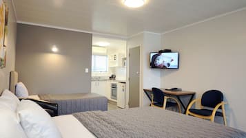 A hotel room with two beds, a desk with chairs, a television, and a kitchenette.