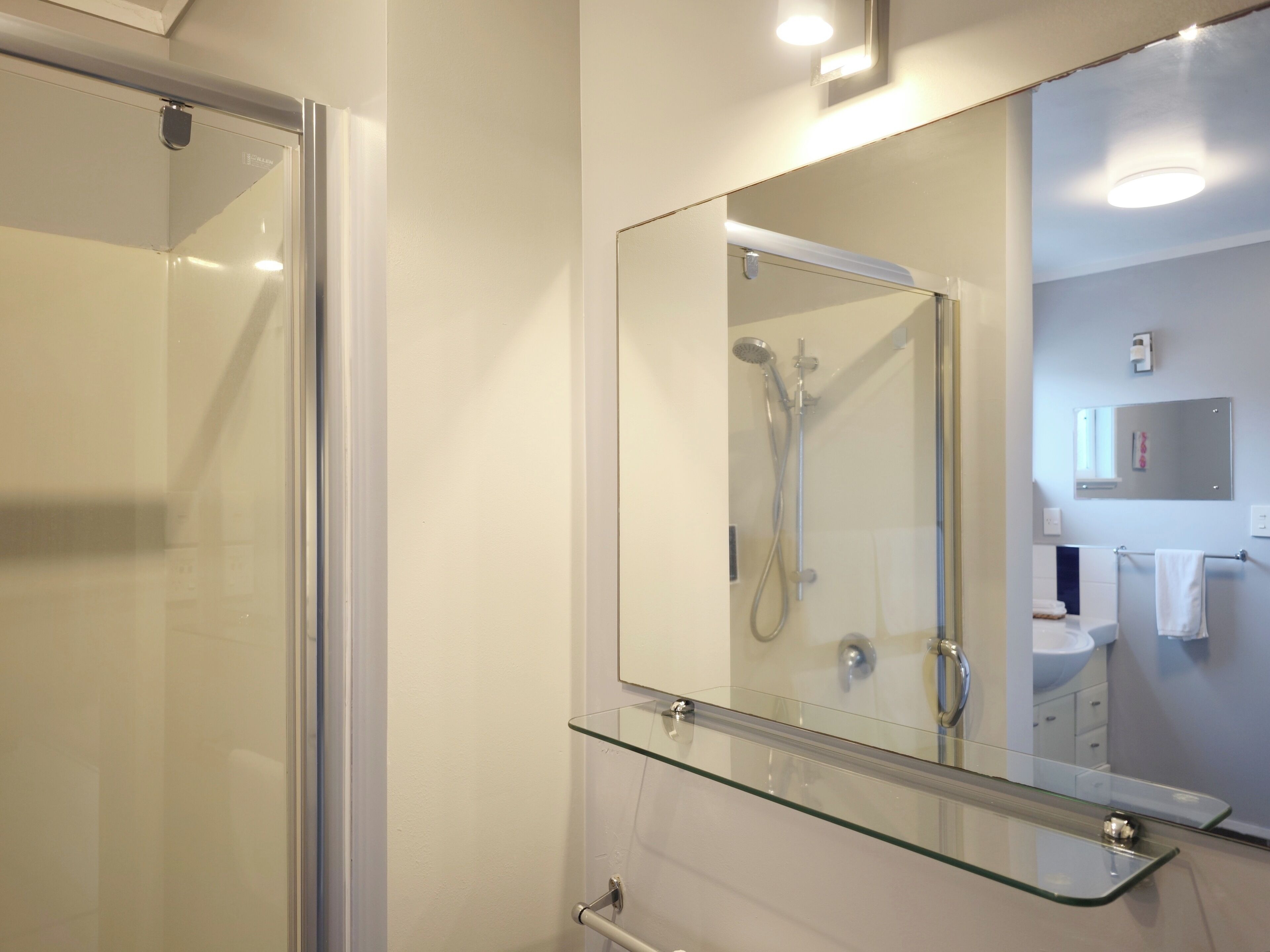 A modern bathroom with a glass shower enclosure, a glass-topped vanity, and a large mirror.