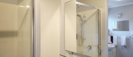 A modern bathroom with a glass shower enclosure, a glass-topped vanity, and a large mirror.