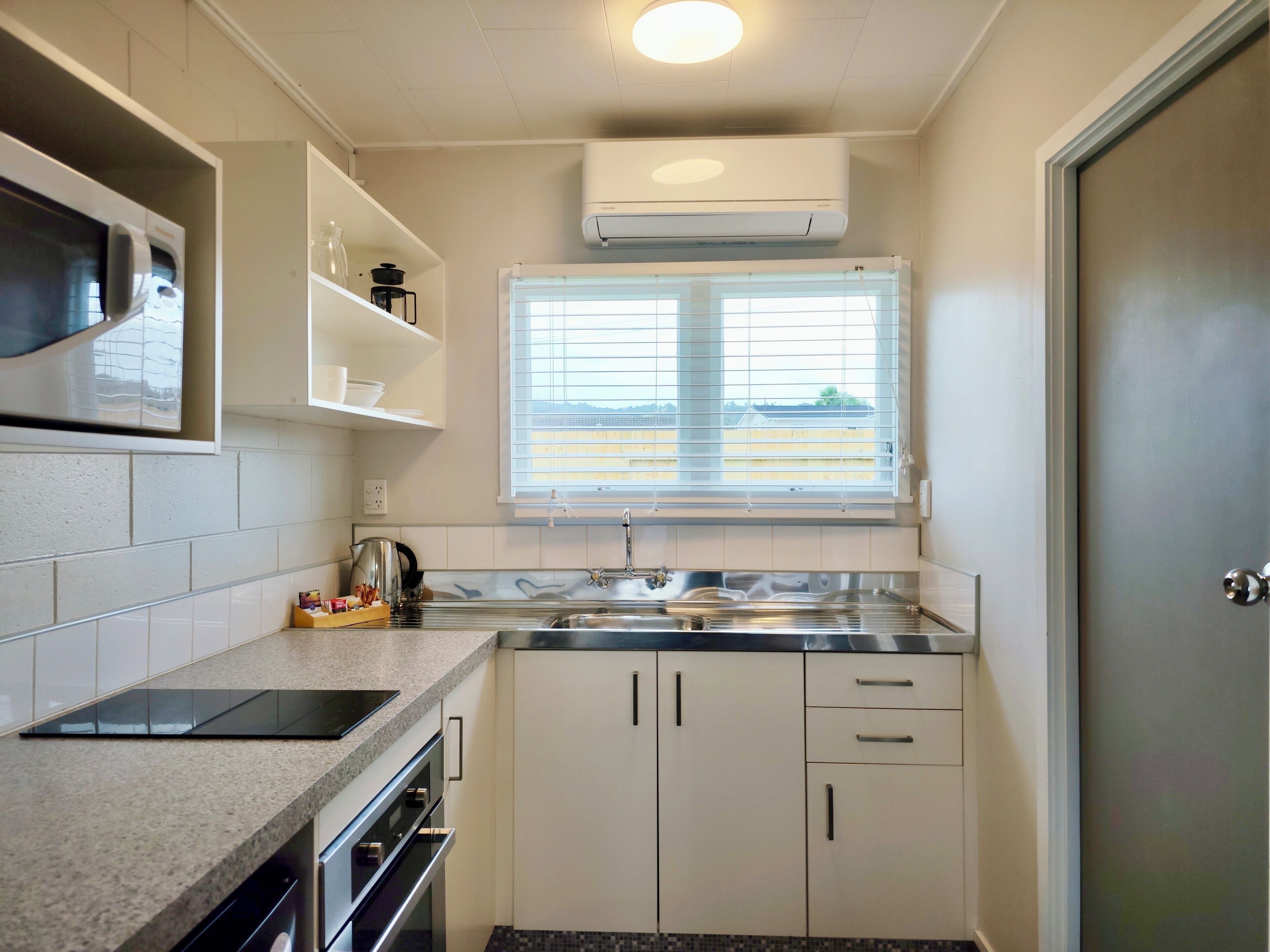 A modern kitchen with a built-in oven, a microwave, a sink, and a window with blinds.