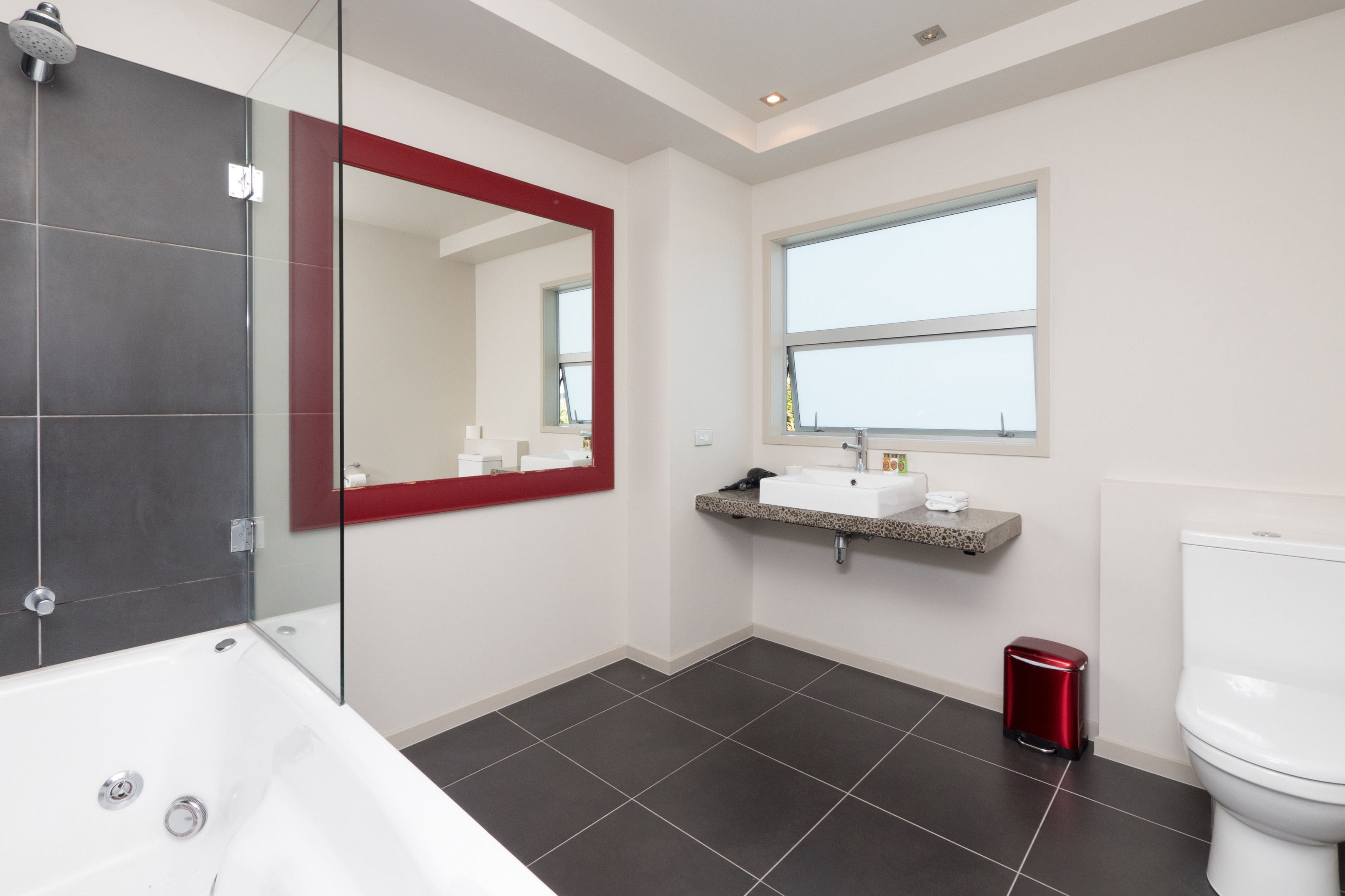 A modern bathroom with a glass-enclosed shower, a large mirror, a sink with a granite countertop, and a toilet.
