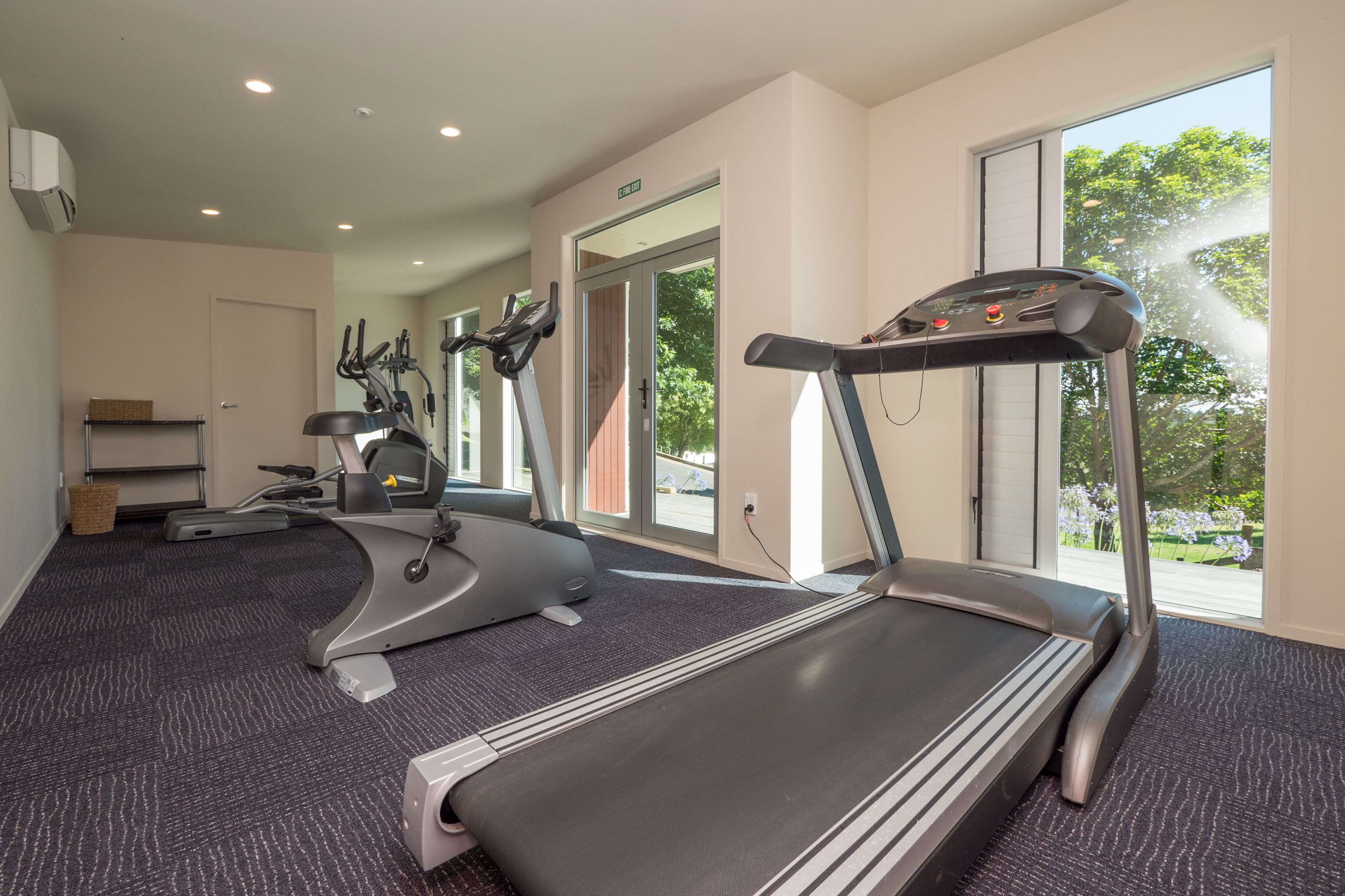A fitness room with treadmills, exercise bikes, and a large window providing a view of the outdoors.