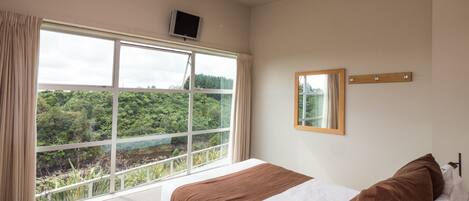 A bedroom with a large window, a bed, a mounted TV, and a mirror on the wall.