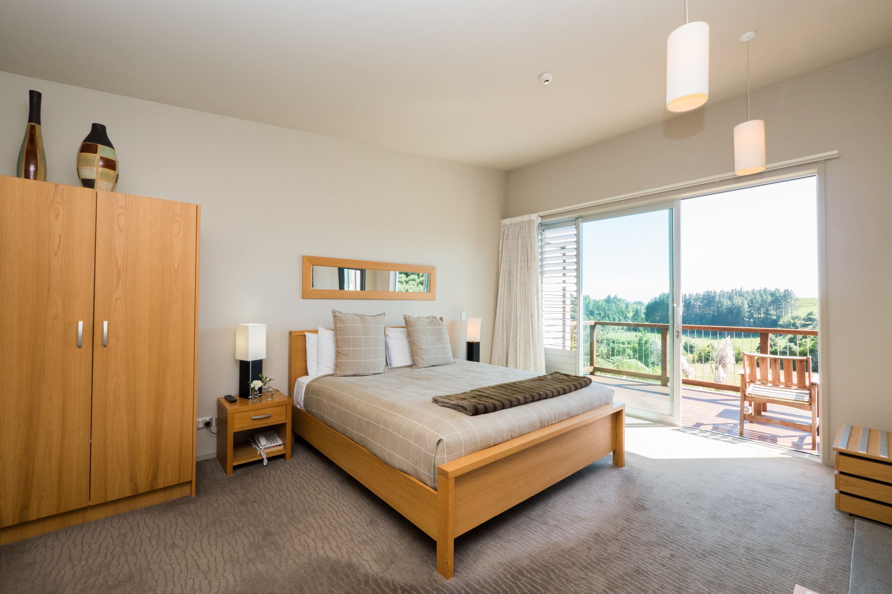 Quarto com cama de madeira, mesas de cabeceira, guarda-roupa e varanda com vista.