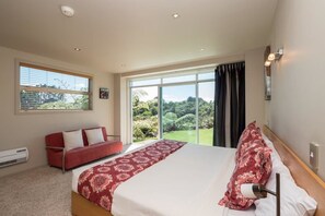 A bedroom with a large bed, a red sofa, a window with a view of greenery, and a ceiling light. - One Burgess Hill (Burgess Park)
