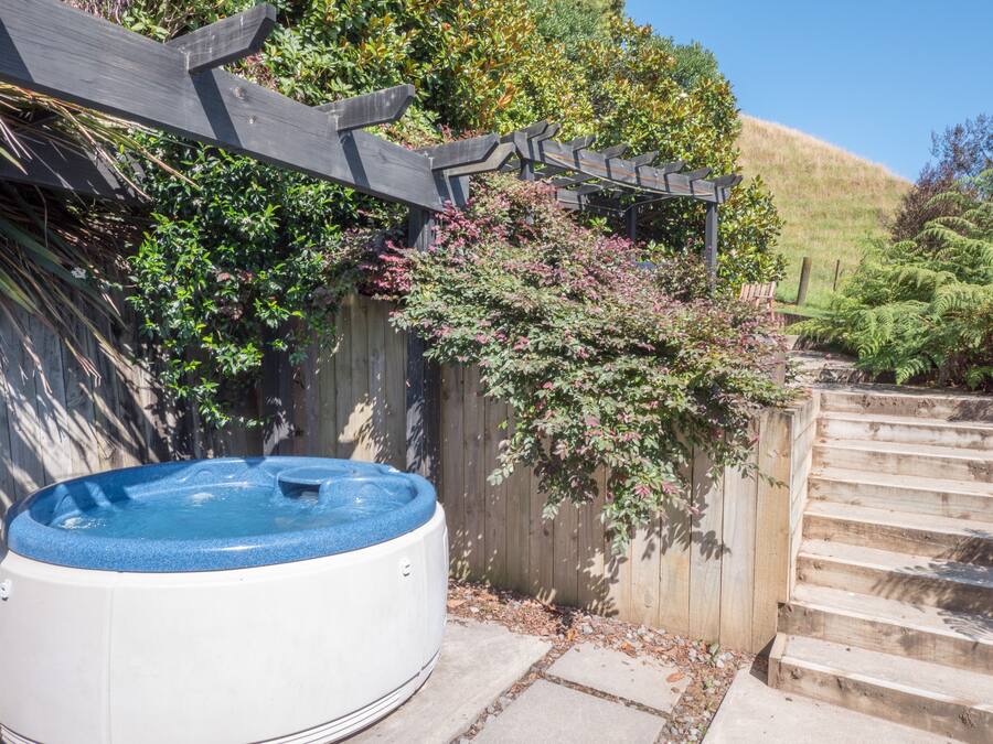 Jacuzzi al pati d'una casa amb una pèrgola de fusta, escales i vegetació abundant.