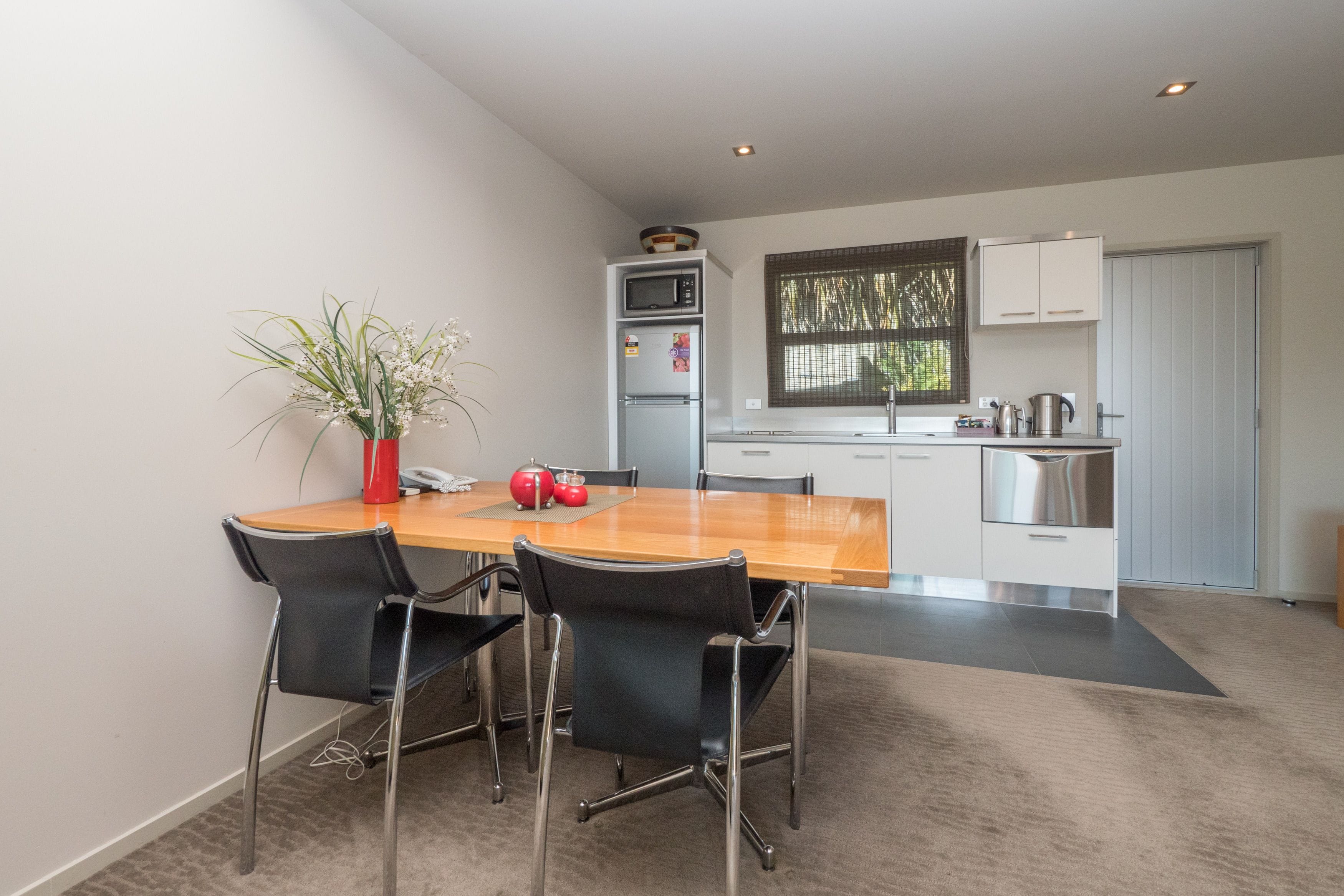 A modern kitchen with a wooden dining table, black chairs, and a potted plant.