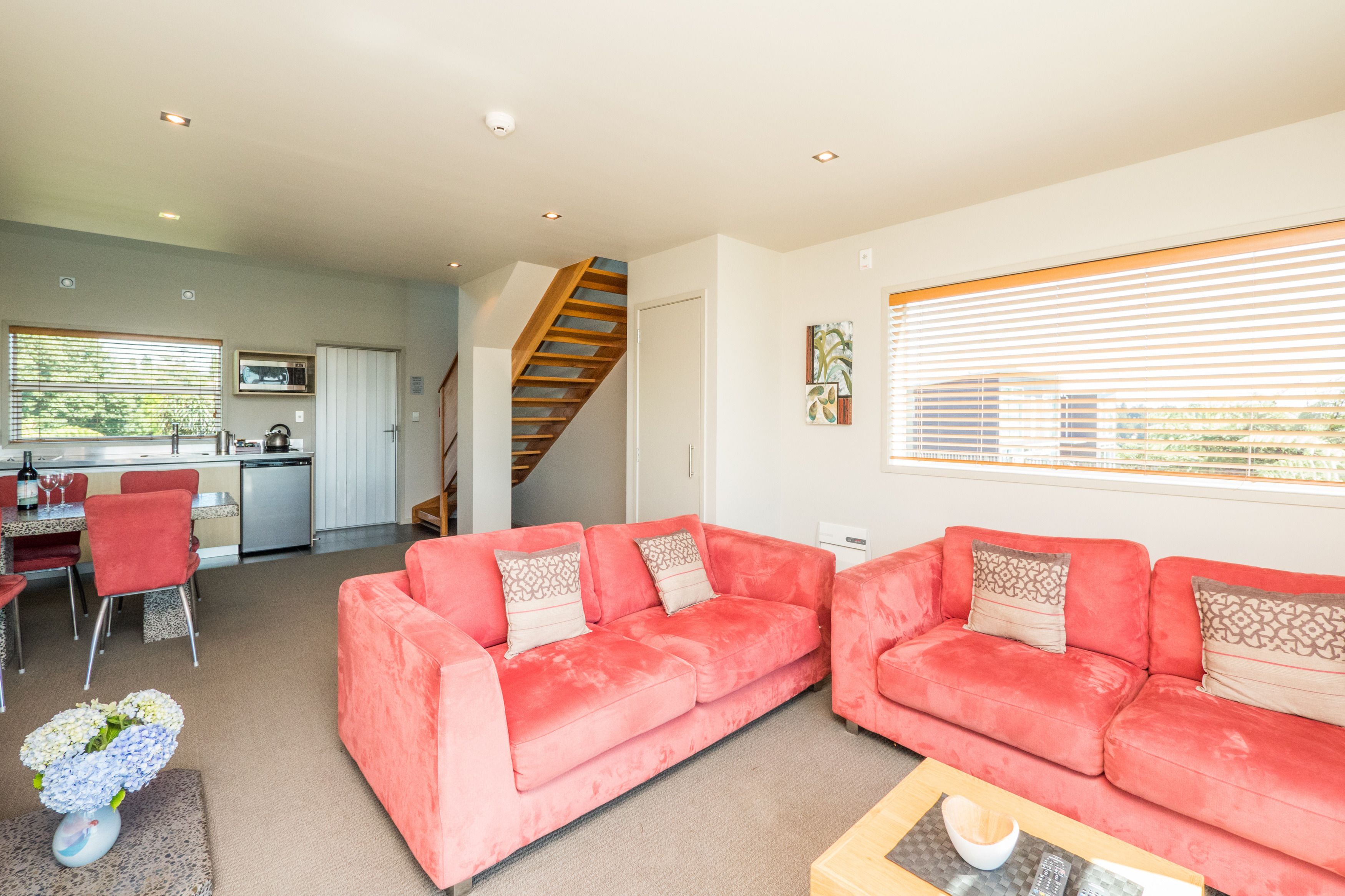 A living room with two red sofas, a wooden coffee table, and a dining area with a kitchen in the background.
