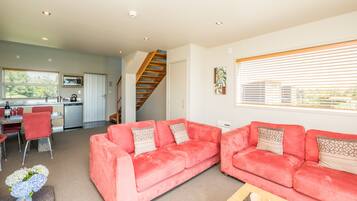 A living room with two red sofas, a wooden coffee table, and a dining area with a kitchen in the background.