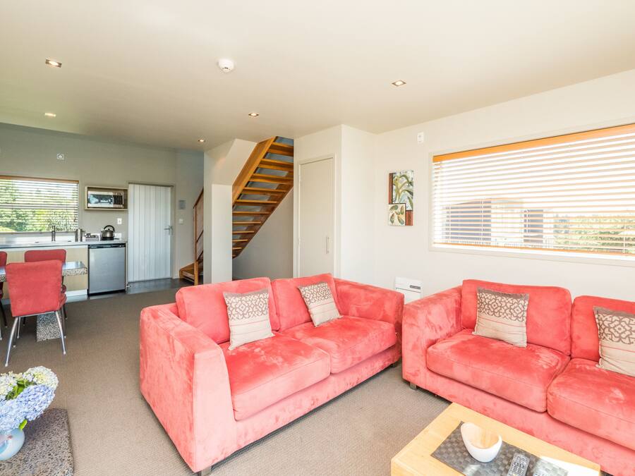 A living room with two red sofas, a wooden coffee table, and a dining area with a kitchen in the background.