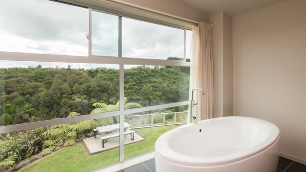 Un baño con una bañera grande, una ventana que ofrece vistas de un paisaje verde exuberante, y una banca al lado de la ventana.