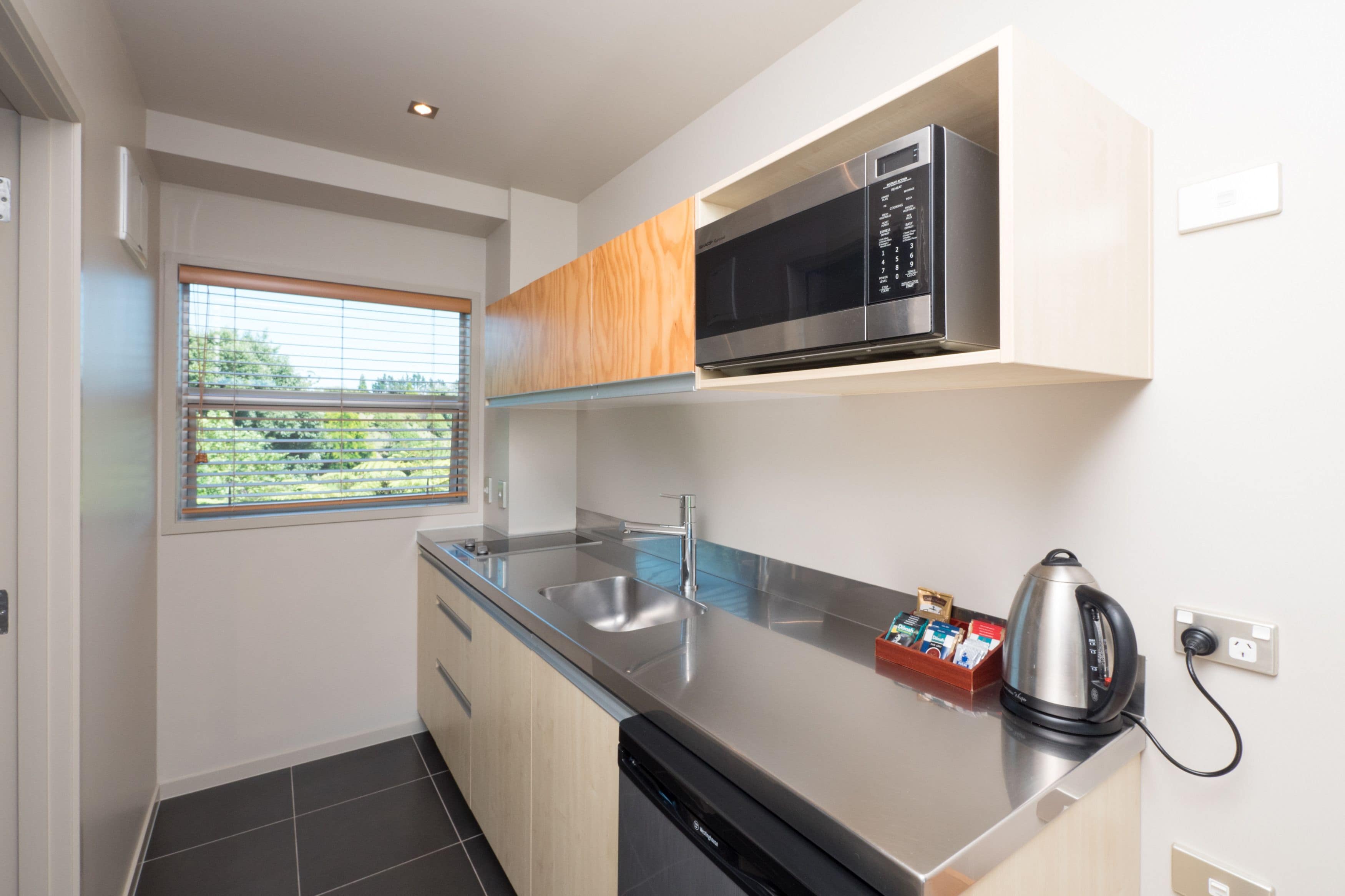 A modern kitchen with a stainless steel microwave, a kettle, and a dish rack.