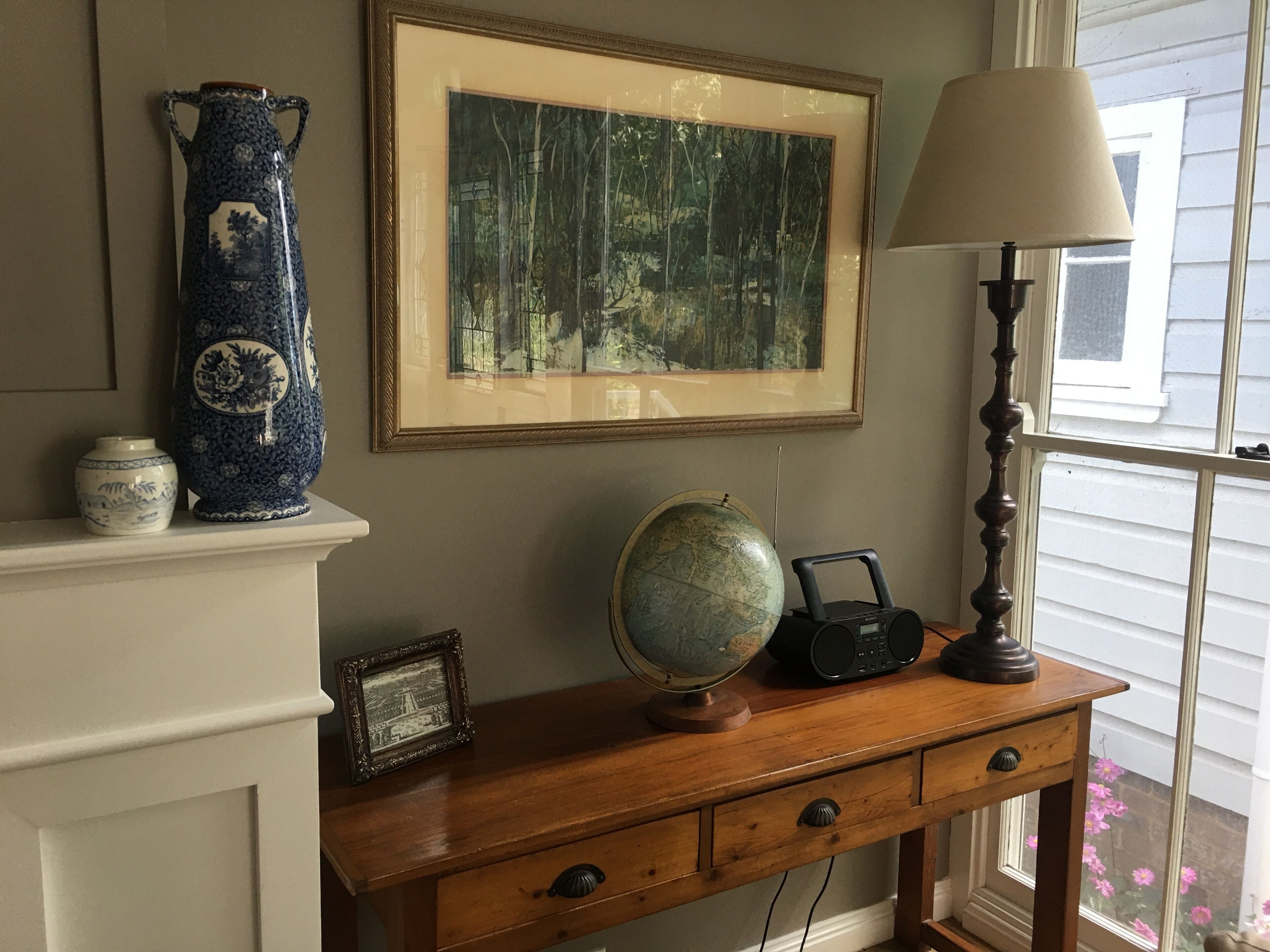 A wooden desk with a globe, radio, framed picture, and decorative vases.