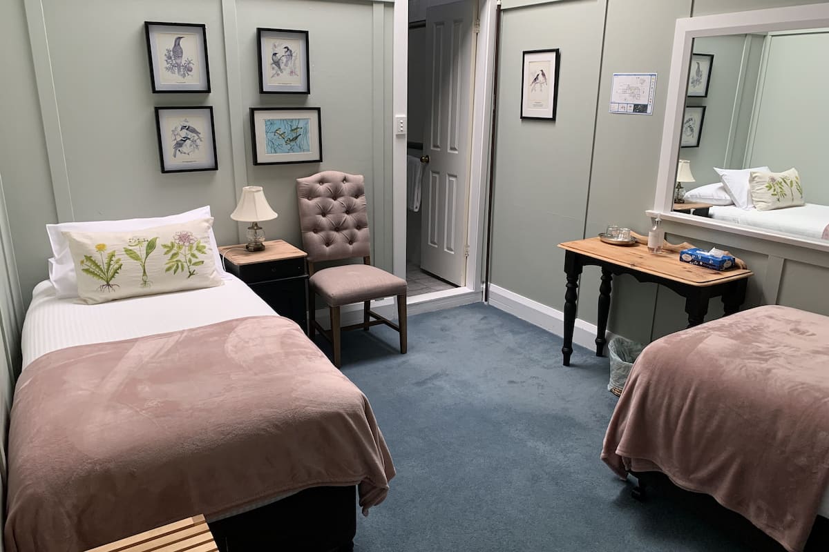 A hotel room with two beds, a chair, a table with toiletries, and framed artwork on the walls.