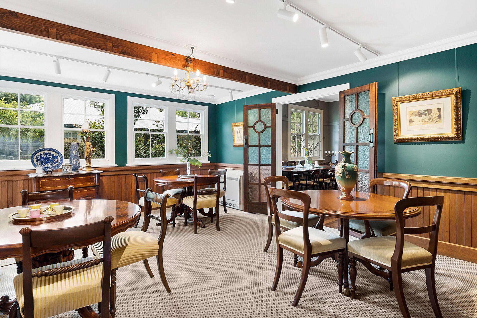 A dining room with wooden furniture, a chandelier, and large windows with views of greenery.