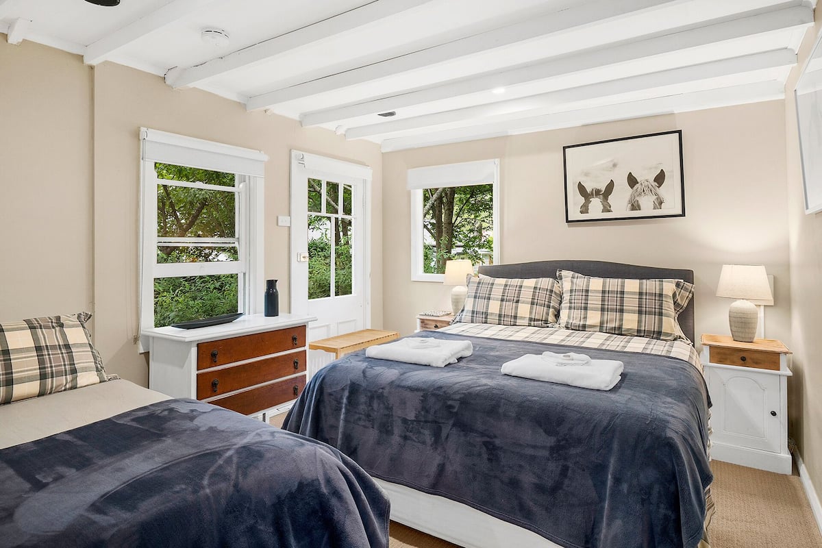 A bedroom with two beds, a wooden bench, a dresser, and a door leading to a garden.