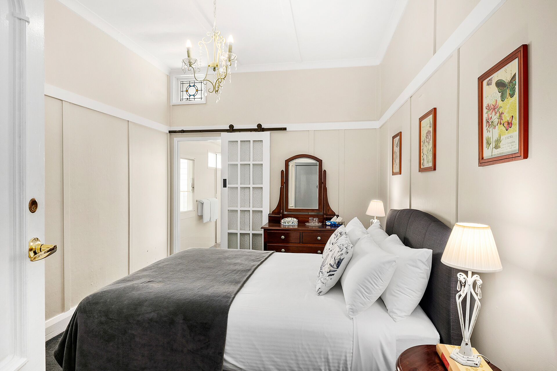 A bedroom with a bed, a dresser, a mirror, a chandelier, and framed artwork on the walls.