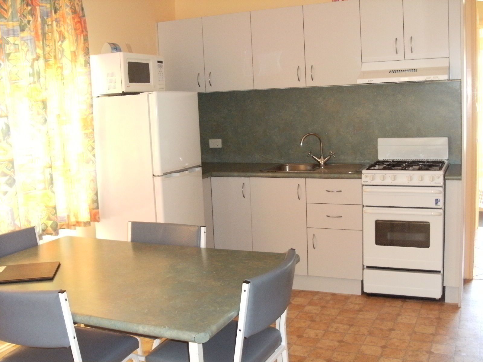 A compact kitchen with white cabinets, a microwave, a sink, and a stove.
