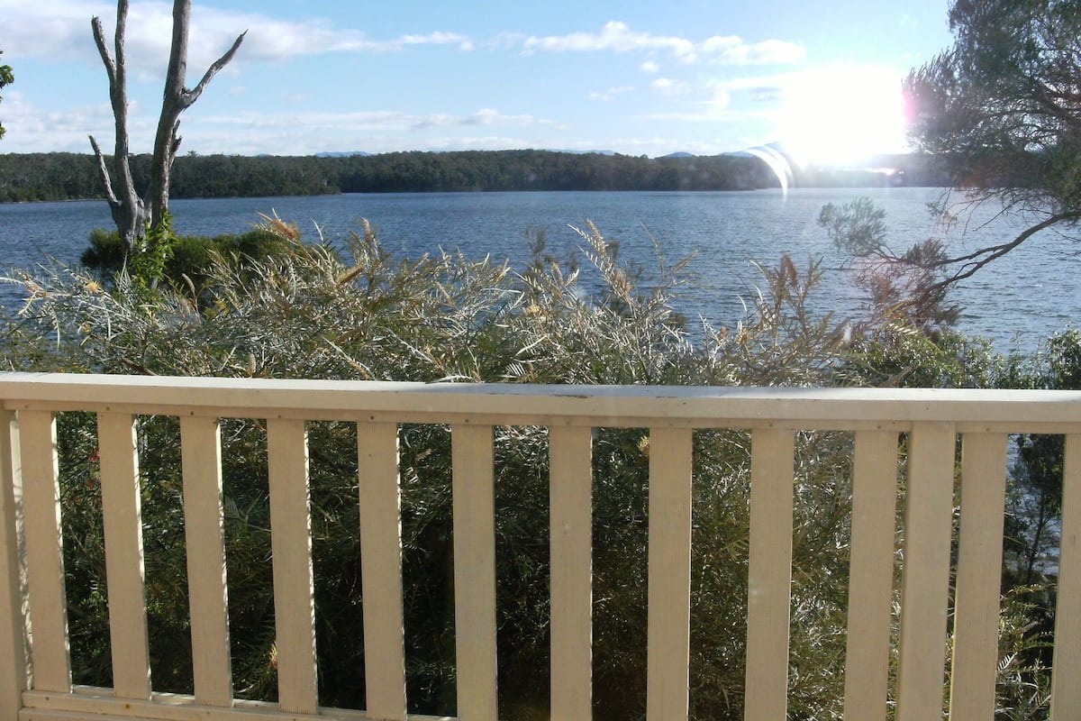 A wooden deck overlooking a lake with trees and shrubs in the foreground.