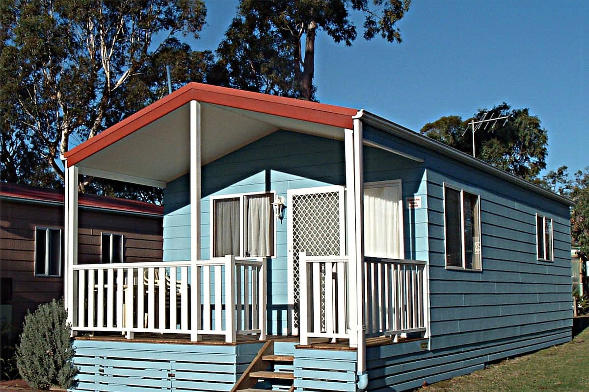 A single-story mobile home with a porch, a small front yard, and a neighboring house.