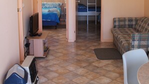 Una habitación pequeña con una cama nido, un escritorio con computadora, un televisor, un sofá y un ventilador de techo.