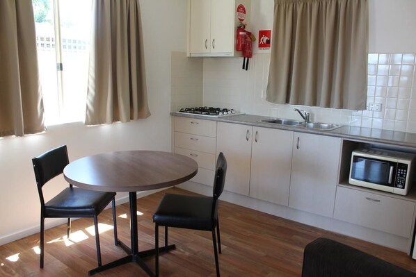 Una cocina moderna con una mesa redonda, dos sillas, estufa a gas, microondas y un lavabo.