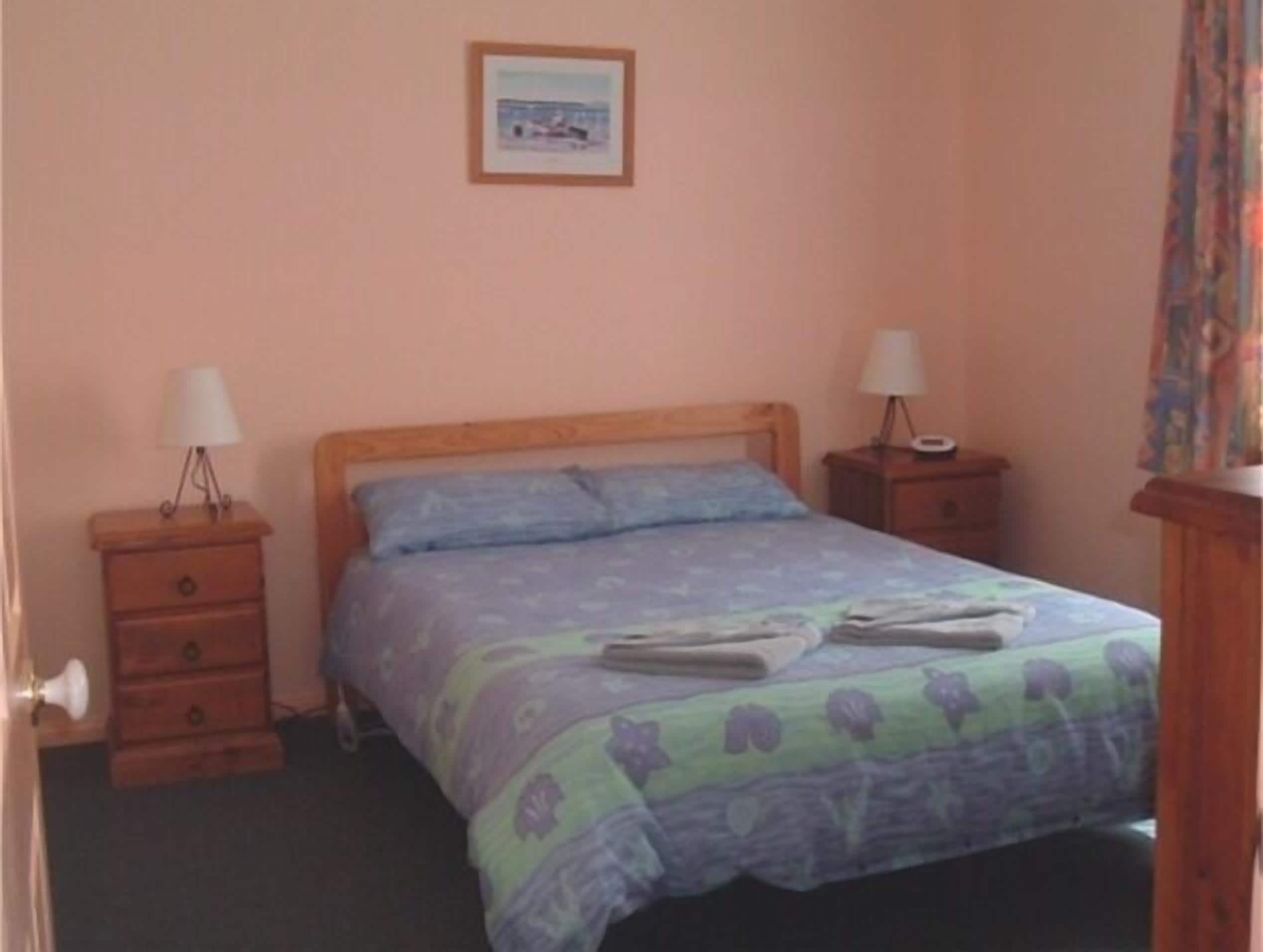 A bedroom with a bed, two bedside tables, a nightstand, a lamp, and a framed picture on the wall.