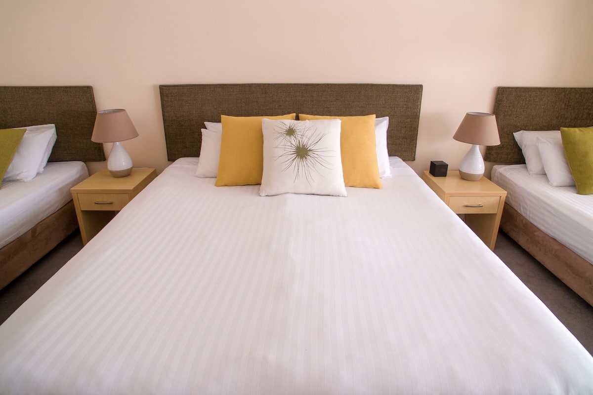 A double bed with a headboard, two bedside tables with lamps, and a nightstand with a lamp.