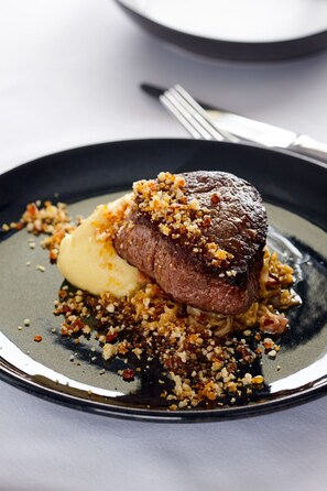 A steak with a crumbly topping and a scoop of mashed potatoes on a plate.