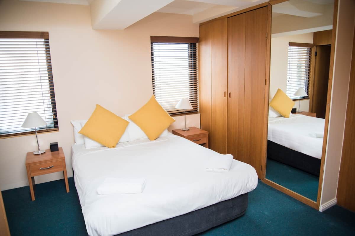 A neatly arranged hotel room with a large bed, two bedside tables, a wardrobe, and a mirror.