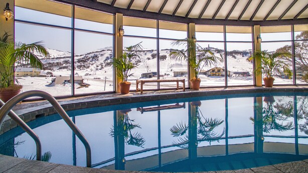 An indoor swimming pool with a view of a snowy landscape through large windows. - Marritz Hotel (Perisher Valley)