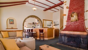 A cozy living area with a sofa, a wooden table, and a fireplace. There is a bar area with stools and a counter. - Marritz Hotel (Perisher Valley)