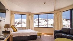 A hotel room with a bed, a sofa, a chair, and a desk with a lamp and books. - Marritz Hotel (Perisher Valley)