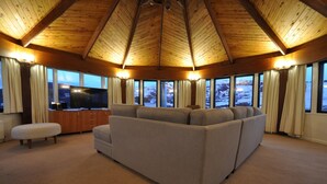 A cozy living room with a large sectional sofa, a flat-screen TV, and a wooden ceiling. - Marritz Hotel (Perisher Valley)