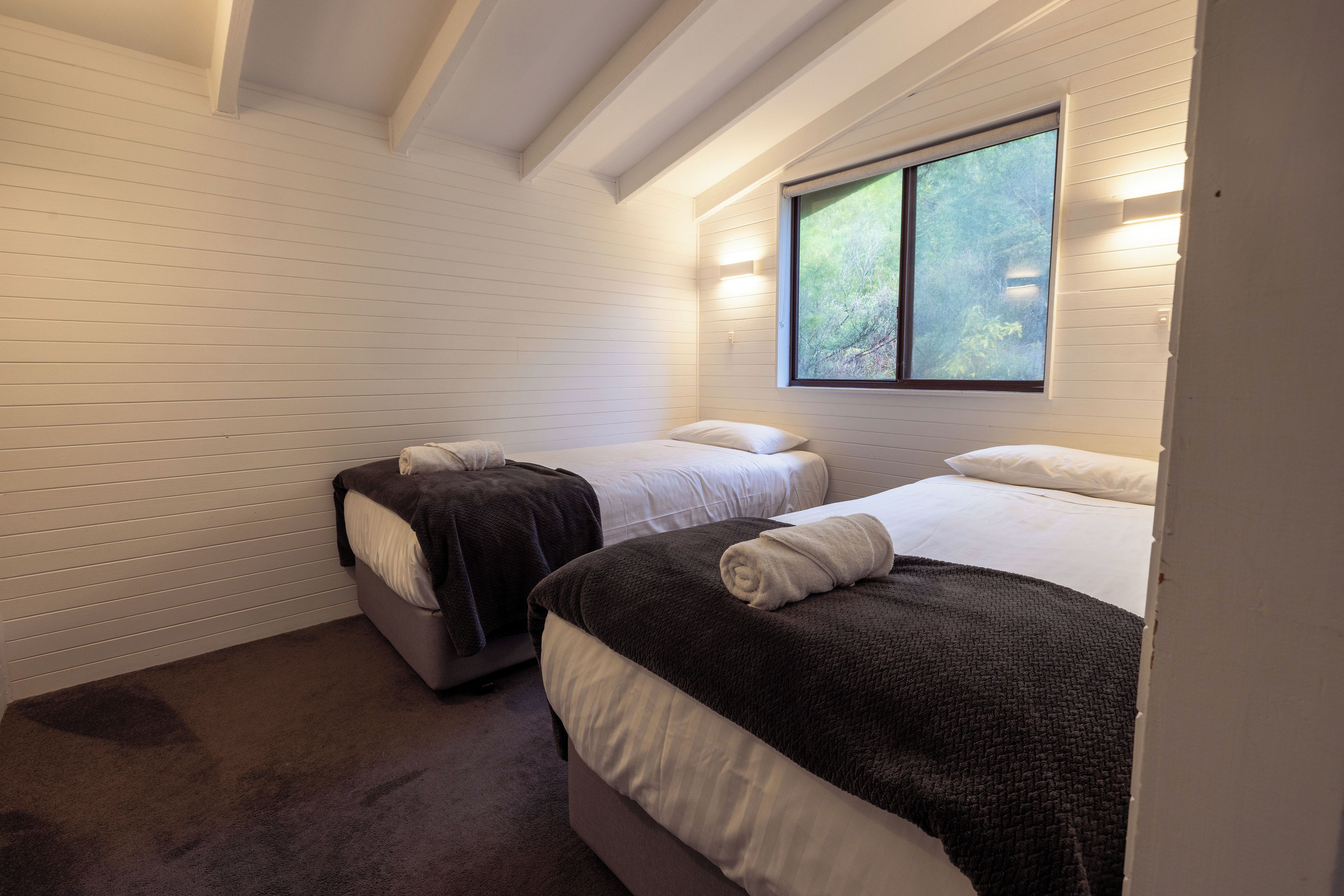 Un dormitorio con dos camas, paredes blancas y una ventana con vistas a árboles.