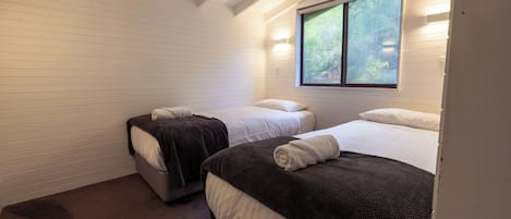 A bedroom with two beds, white walls, and a window with a view of trees.