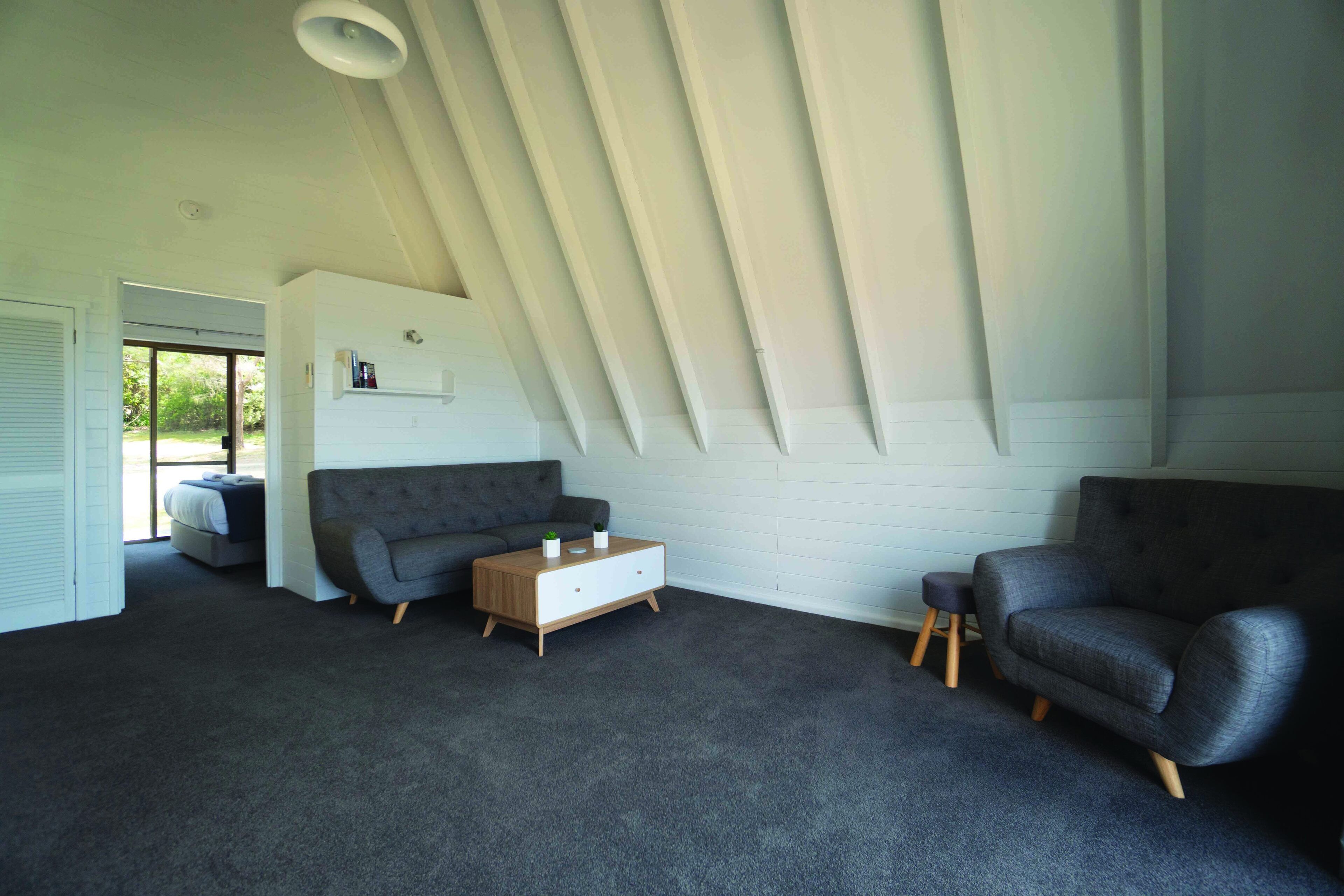 Een moderne woonkamer met een schuine kap, een grijze bank, een houten salontafel en een grijze fauteuil.