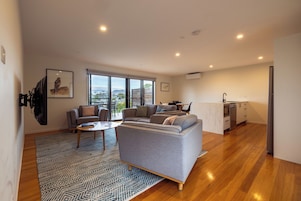 Una sala moderna con un sofá, una mesa de centro y un televisor. Hay una zona de cocina con un refrigerador y un lavavajillas.