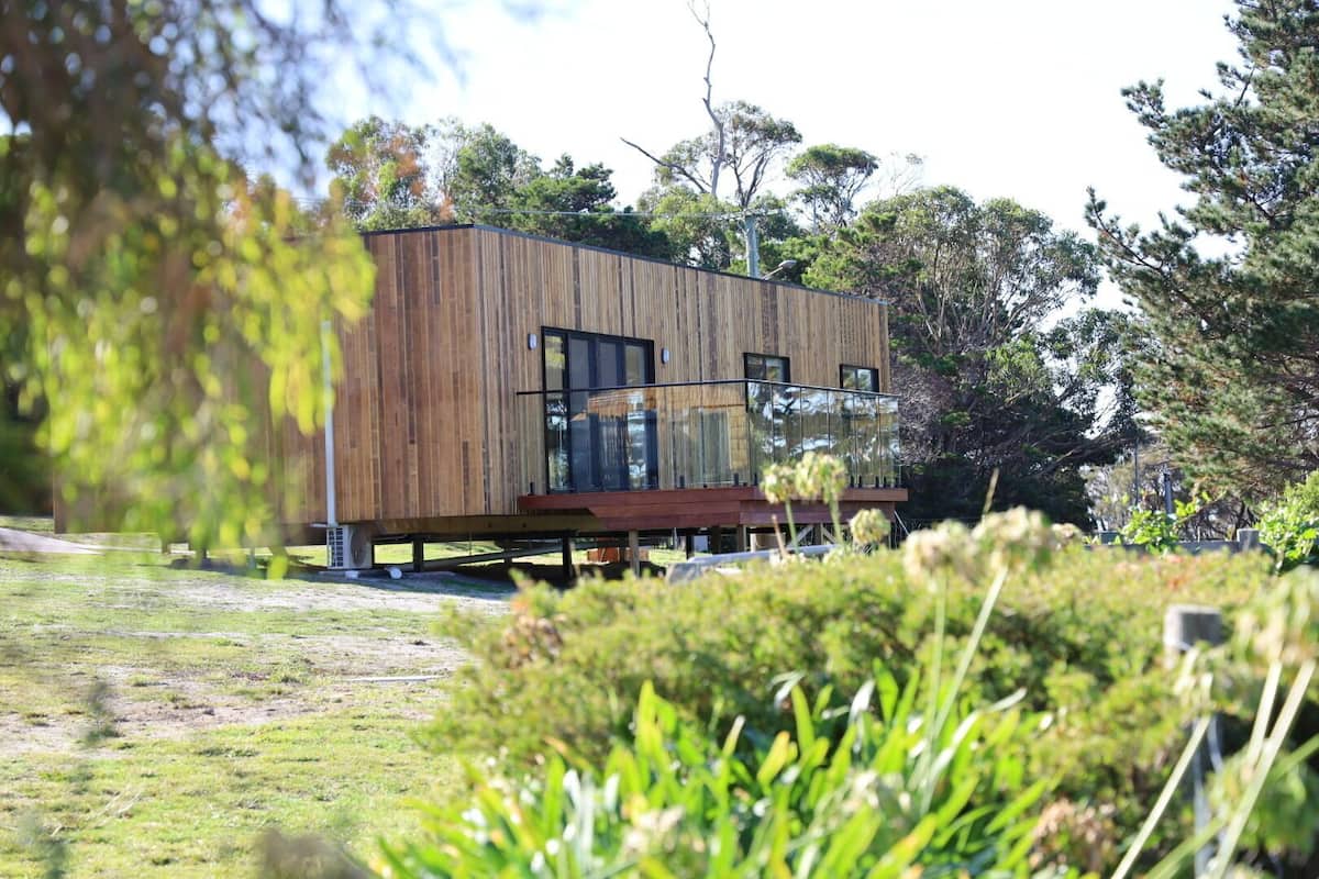 Una cabaña moderna de madera con terraza, rodeada de exuberante vegetación y árboles.