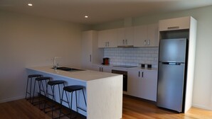 Una cocina moderna con una isla central, taburetes de bar, un refrigerador de acero inoxidable y armarios blancos.