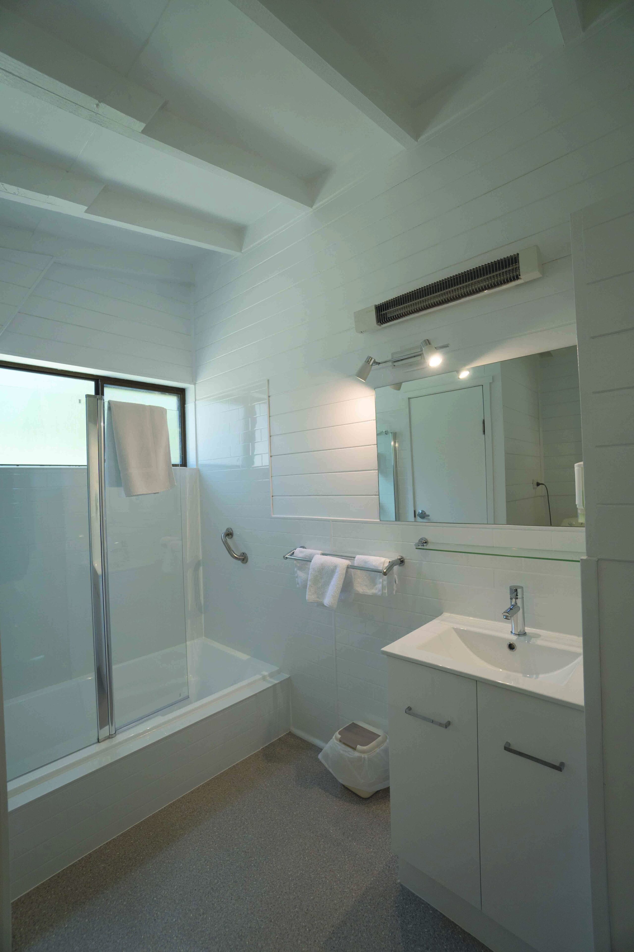 Un bagno moderno con cabina doccia in vetro, lavabo bianco e uno specchio grande.