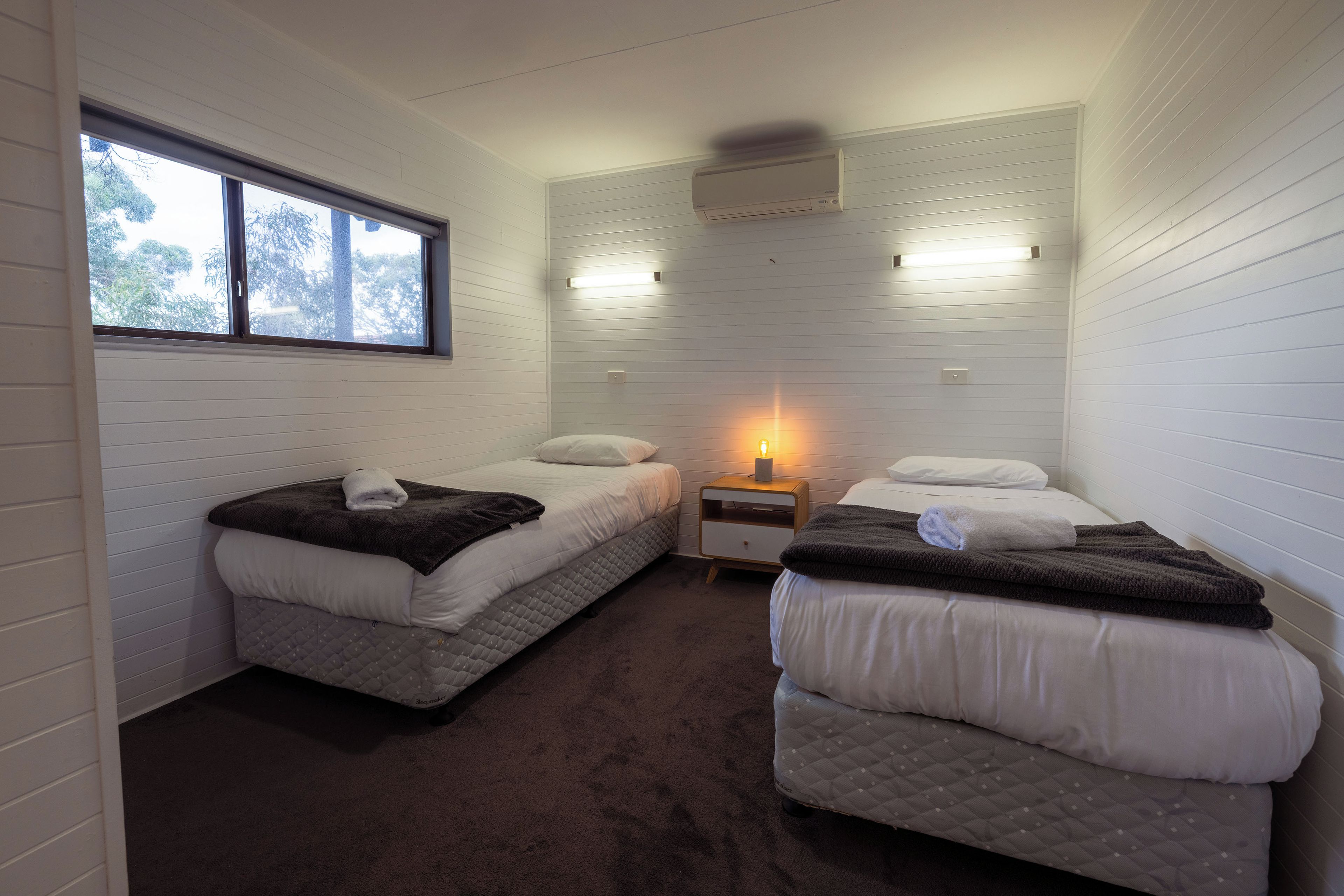 Une chambre avec deux lits simples, une table de chevet avec une lampe et une fenêtre.